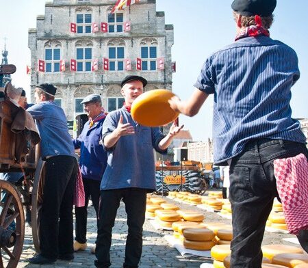 Traditionele Goudse Kaasmarkt in Gouda, waar kaasdragers in historische klederdracht grote kazen verhandelen op het marktplein voor het Stadhuis.