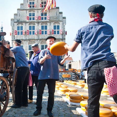 Traditionele Goudse Kaasmarkt in Gouda, waar kaasdragers in historische klederdracht grote kazen verhandelen op het marktplein voor het Stadhuis.